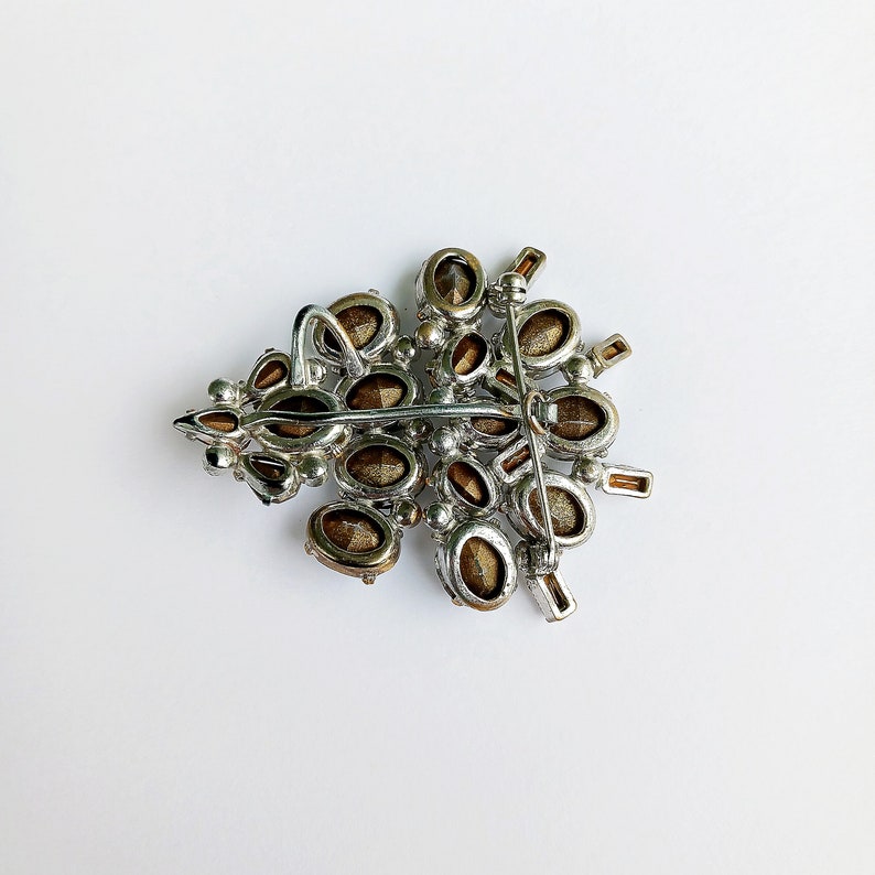 May include: A silver tone brooch with a cluster of brown rhinestones in the shape of a tree. The brooch has a pin back.