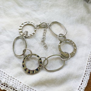 Op de afbeelding: Een zilveren armband met meerdere met elkaar verbonden cirkels in verschillende maten. De cirkels hebben een getextureerde, gehammerde afwerking.