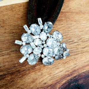 May include: A silver-toned brooch with a cluster of clear rhinestones arranged in a floral pattern.