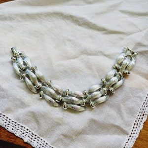 May include: A silver bracelet with a unique, interlocking design. The bracelet is made of multiple linked, elongated, oval-shaped pieces.