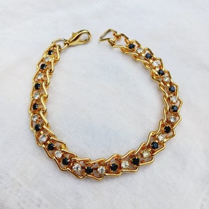 May include: A gold chain bracelet with alternating black and white rhinestones.