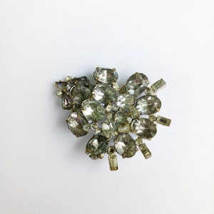 May include: A vintage brooch with a cluster of clear and gray rhinestones set in silver tone metal.