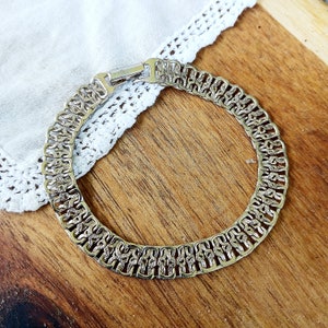 Puede incluir: Collar de cadena plateado con un diseño detallado e intrincado. El collar está hecho de piezas de metal enlazadas que forman un patrón repetitivo.