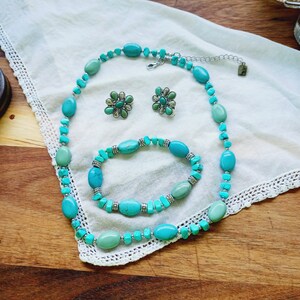 May include: A turquoise and silver necklace, bracelet, and earrings set. The jewelry features oval-shaped turquoise stones and silver accents.