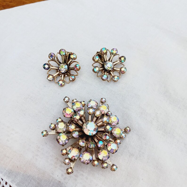 K&ouml;nnte beinhalten: Ein Vintage-Set aus schimmerndem Strassschmuck mit einer gro&szlig;en Brosche und einem Paar Ohrringen. Die Brosche ist sternf&ouml;rmig mit einem Strass-Cluster in der Mitte. Die Ohrringe sind kleiner und haben ein &auml;hnliches Design.