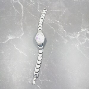 May include: A silver wristwatch with a pale face and a linked strap. The watch features a simple, elegant design, with a round face and a clasp. The watch is a classic accessory, suitable for everyday wear.