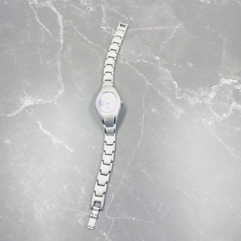 May include: A silver wristwatch with a pale face and a linked strap. The watch features a simple, elegant design, with a round face and a clasp. The watch is a classic accessory, suitable for everyday wear.