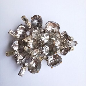 May include: A silver brooch with a cluster of clear rhinestones in various shapes and sizes.