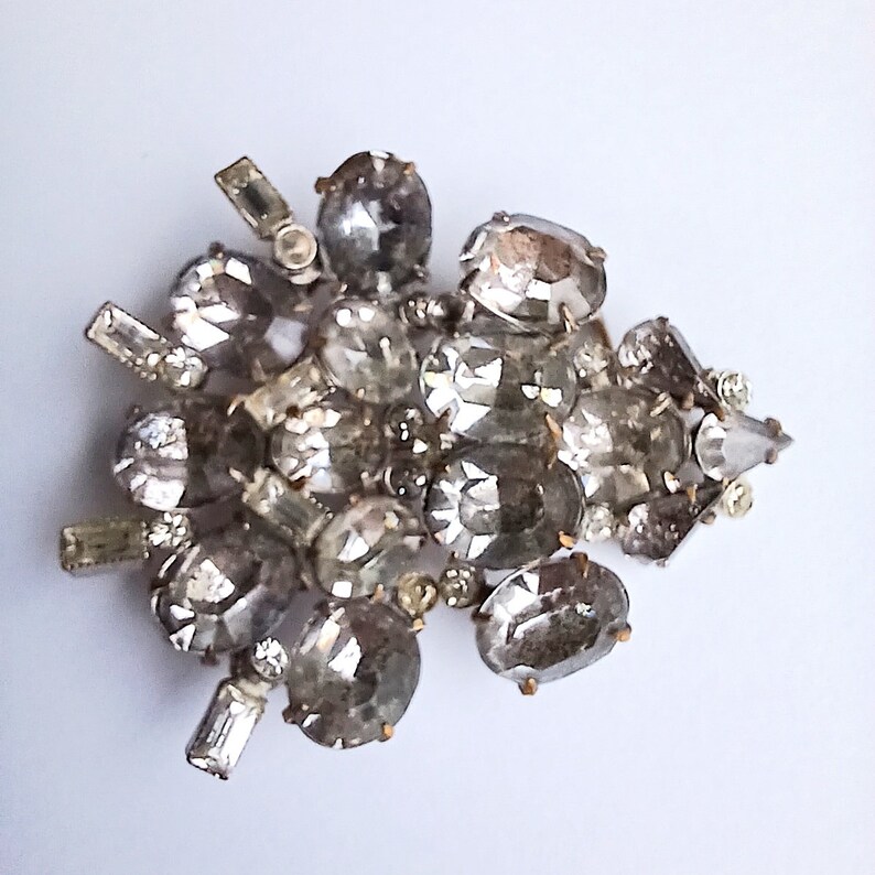 May include: A silver brooch with a cluster of clear rhinestones in various shapes and sizes.