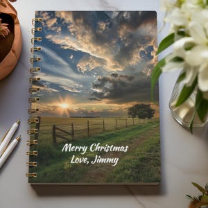 May include: A spiral bound notebook with a scenic sunset landscape on the cover. The text "Merry Christmas Love, Jimmy" is printed on the bottom of the cover.