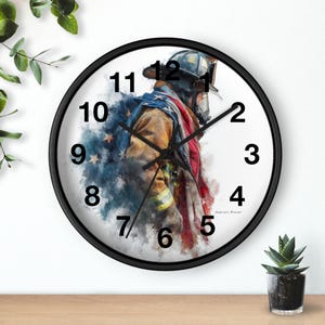 Puede incluir: Reloj de pared redondo negro con una ilustración de acuarela de un bombero con uniforme, con un diseño de bandera americana. La esfera del reloj tiene números y manecillas negras. El reloj está sobre una superficie de madera.