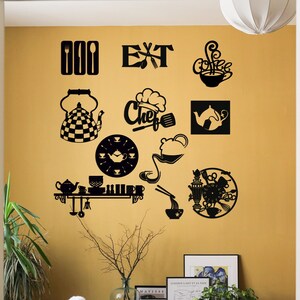 May include: A dining room with a yellow wall decorated with black metal wall art featuring kitchen-themed designs, including a teapot, a clock, and the word "Chef". The wall art is arranged in a grid pattern. There is a wooden table with two white chairs, a wooden bench with a vase of flowers, and a potted plant in the room.
