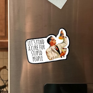 May include: A refrigerator magnet with a retro illustration of a scientist holding a beaker. The magnet has the text "LET'S FIND A CURE FOR STUPID PEOPLE" in white letters. The magnet is black and white with orange and yellow accents.