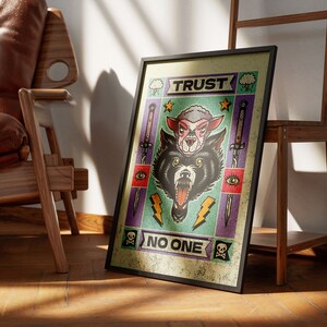 May include: A framed print with a colorful illustration of a wolf's head with a sheep's head inside. The print has the text "TRUST NO ONE" in a banner at the bottom.
