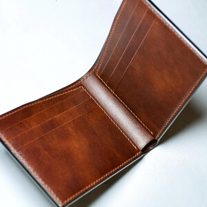 May include: Open brown leather wallet with multiple card slots and a bill compartment. The wallet is made of smooth, high-quality leather with visible stitching around the edges. The interior is a lighter shade of brown than the exterior.