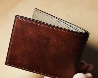 May include: A brown leather wallet with a stitched edge and a light brown interior.