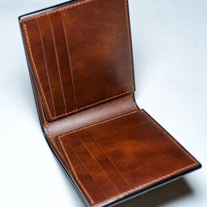 May include: Open brown leather wallet with multiple card slots. The wallet is made of smooth, high-quality leather and features detailed stitching around the edges. The interior is a lighter shade of brown, with several compartments for cards and cash.