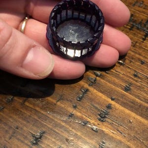 Peut inclure: Un bouchon de bouteille en plastique violet avec un motif décoratif. Le bouchon est rond et possède un bord surélevé.