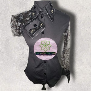 Peut inclure: Une chemise boutonnée noire avec une superposition de dentelle sur les manches. Le col est orné de strass noirs et de perles. La chemise a une silhouette ajustée et un logo qui dit "The Aztec Couture, Ride in What You Believe".