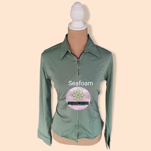 May include: Seafoam green long-sleeve shirt with a zipper closure and a collared neckline. The shirt has a fitted silhouette and is made of a soft, comfortable fabric. The text "THE AESTHETIC COUTURE" is printed on the shirt.