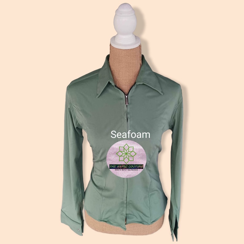 May include: Seafoam green long-sleeve shirt with a zipper closure and a collared neckline. The shirt has a fitted silhouette and is made of a soft, comfortable fabric. The text "THE AESTHETIC COUTURE" is printed on the shirt.