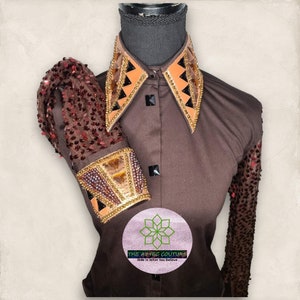 Può includere: Una camicia marrone a maniche lunghe con un colletto e polsini decorativi. Il colletto è in pelle marrone con disegni geometrici dorati e neri. I polsini sono in tessuto marrone con disegni geometrici dorati e neri. La camicia ha un logo in basso che dice "The Aztec Couture, Ride in What You Believe".