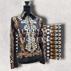 May include: A black show jacket with brown and silver embroidery and rhinestones. The jacket has a zipper closure and long sleeves. The text "The Aztec Couture" is visible on the jacket. A brown and white patterned fabric is visible in the background.