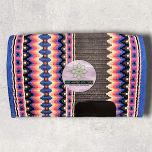 Op de afbeelding: Een rechthoekig paardenzadeldek met een blauwe rand en een grijs middenstuk. Het dek heeft een kleurrijk geometrisch patroon in roze, blauw, zwart en wit. Een zwart leren patch zit aan de onderkant. Het Aztec Couture-logo is zichtbaar.