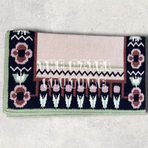May include: A pink and black saddle pad with a floral design. The pad has a green border and the text "The Grazing Couture" is embroidered in white.