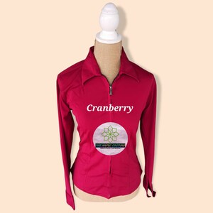 May include: A cranberry colored long-sleeved shirt with a zipper closure. The shirt has a collar and is fitted. The text "Cranberry" and "The Aztec Couture" is printed on the shirt.