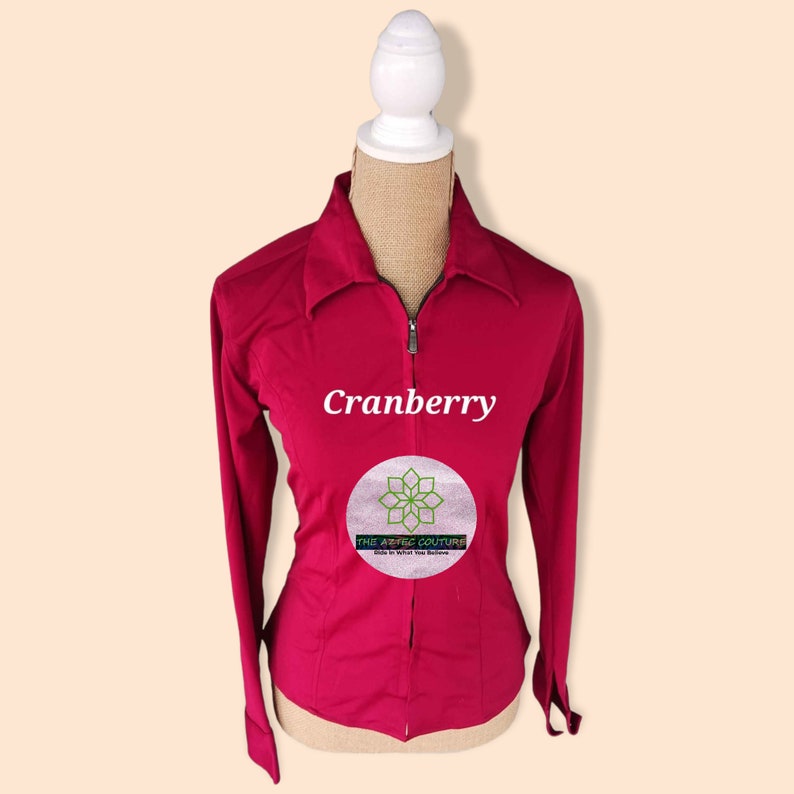 May include: A cranberry colored long-sleeved shirt with a zipper closure. The shirt has a collar and is fitted. The text "Cranberry" and "The Aztec Couture" is printed on the shirt.