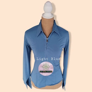 May include: Light blue long-sleeved collared shirt with a zipper closure. The shirt has a fitted silhouette and is made of a smooth fabric. The text "THE AESTHETIC COUTURE" is printed on the shirt.