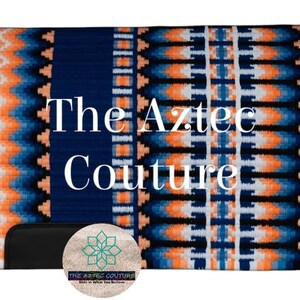 Op de afbeelding: Een marineblauwe paardenzadeldek met een op de Azteken geïnspireerd ontwerp in oranje, wit en blauw. De tekst "The Aztec Couture" wordt in het wit weergegeven. Een zwart object en een cirkelvormig logo staan onderaan.