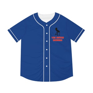May include: A blue baseball jersey with white trim and a white collar. The jersey has a black and white illustration of a creature with the text "THE DOVER DEMONS" in red.