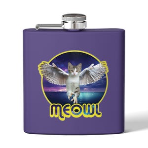 May include: A purple stainless steel hip flask with a quirky design. The design features a cat with owl wings, set against a night sky and ocean backdrop. The word "meowl" is written in yellow and blue. The flask has a silver cap.