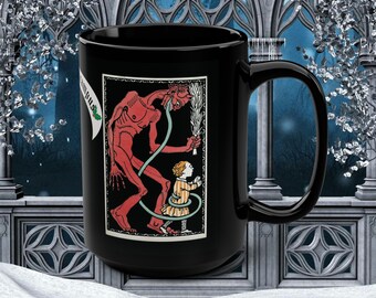 Puede incluir: Taza de cerámica negra con una ilustración roja y negra de una figura diabólica y un niño. La ilustración está enmarcada en un borde blanco. La taza tiene un asa grande y una pancarta blanca con texto.