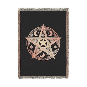 May include: Black woven throw blanket with a large, detailed pentagram design in shades of gold and peach. The pentagram is surrounded by crescent moons, stars, and intricate patterns. The blanket has a fringed edge.