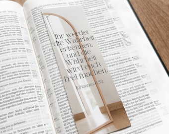 Op de afbeelding: Een close-up van een bijbel die open ligt op een pagina met een bladwijzer. De bladwijzer is een rechthoekige houten vorm met een witte achtergrond en zwarte tekst die "Ihr werdet die Wahrheit erkennen, und die Wahrheit wird euch frei machen. Johannes 8:32" luidt.
