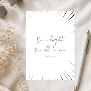 Könnte beinhalten: Eine rechteckige weiße Karte mit schwarzem Text, der Be a light for all to see. Matthew 5:16 lautet. Das Kartendesign enthält dünne, schwarze, strahlenförmige Linien, die von den Rändern zur Mitte verlaufen und einen Strahlenkranzeffekt erzeugen.