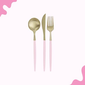 Puede incluir: Un juego de cuchara, cuchillo y tenedor dorados con mangos rosa claro. Los cubiertos están dispuestos verticalmente sobre un fondo blanco con formas abstractas rosas en las esquinas. La cuchara está a la izquierda, el cuchillo en el centro y el tenedor a la derecha.