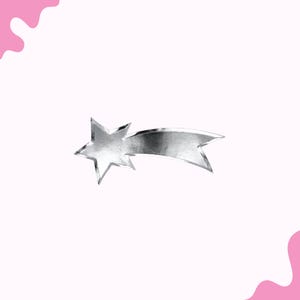 May include: A silver shooting star charm with a five-pointed star and a flowing tail. The charm is set against a soft pink background with a decorative pink shape in the upper left and lower right corners.
