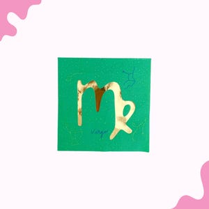 May include: A square, emerald green card with a gold Virgo symbol cut out. The word "Virgo" is written in gold script below the symbol. Constellation outlines are in blue and gold.