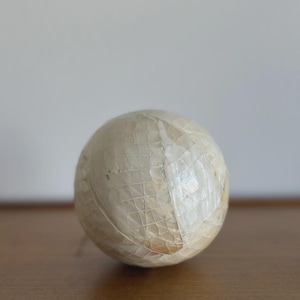 May include: A spherical decorative object with a mosaic-like pattern. The sphere is primarily off-white with a grid-like design, and appears to be made of small, rectangular pieces. The object is resting on a wooden surface.
