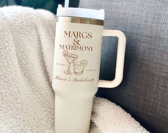 Może przedstawiać: Biały kubek podróżny z brązowym uchwytem i brązowym napisem "Margs & Matrimony Est. 2024 Austin, TX Karen's Bachelorette". Kubek ma białą pokrywkę i słomkę.