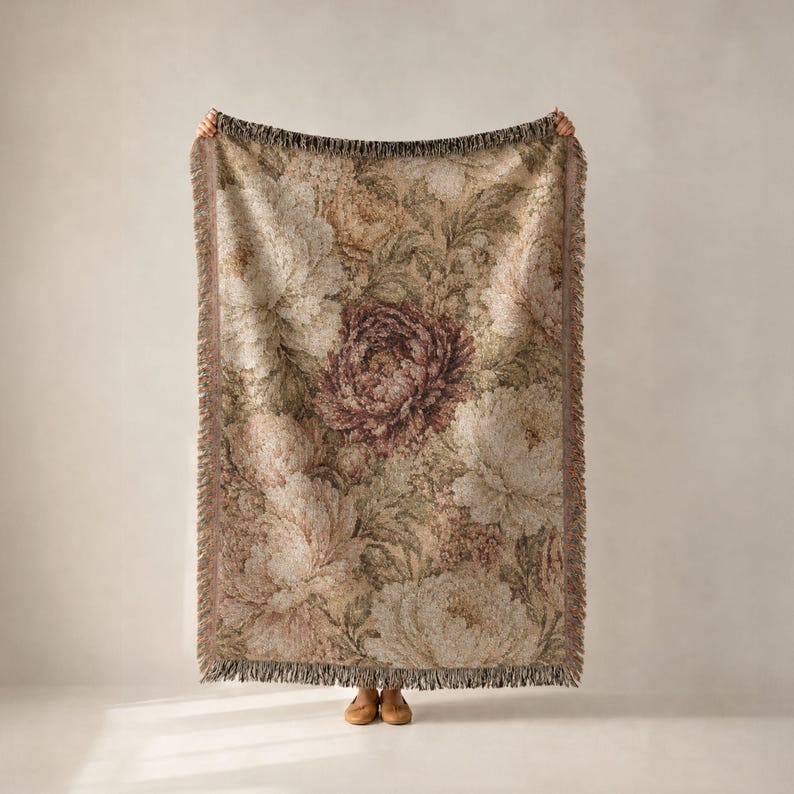 May include: A rectangular woven throw blanket featuring a detailed floral pattern with large, layered peony-like blossoms in shades of muted pink, deep burgundy, cream, and sage green, finished with a decorative fringed edge on all sides.