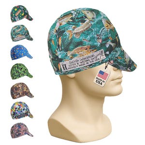 May include: A green welding cap featuring a fish pattern and a white label with the text CUSTOM EXPRESSIONS FITTER & WELDING HATS PROUDLY MADE IN THE USA. A tag attached to the cap displays an American flag and the text MADE IN USA.