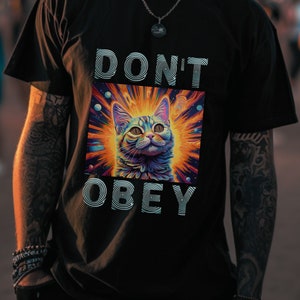 May include: A black t-shirt with a graphic of a cat in a colorful, psychedelic space scene. The text "DON'T OBEY" is printed in white below the image.