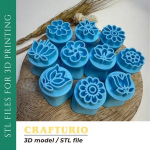 May include: A selection of light blue flower-shaped 3D printing stamps. The stamps are displayed on a wooden surface, with dried wheat stalks in the background. The image includes the text "STL FILES FOR 3D PRINTING" and "CRAFTURIO 3D model / STL file."