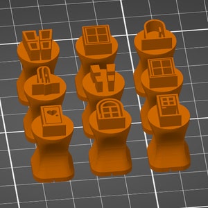 May include: Twelve orange rubber stamps with different designs, including windows, doors, and a heart. The stamps are arranged in three rows of four.