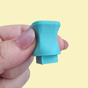 May include: A turquoise blue plastic 3D printed object with a square base and a cylindrical top.
